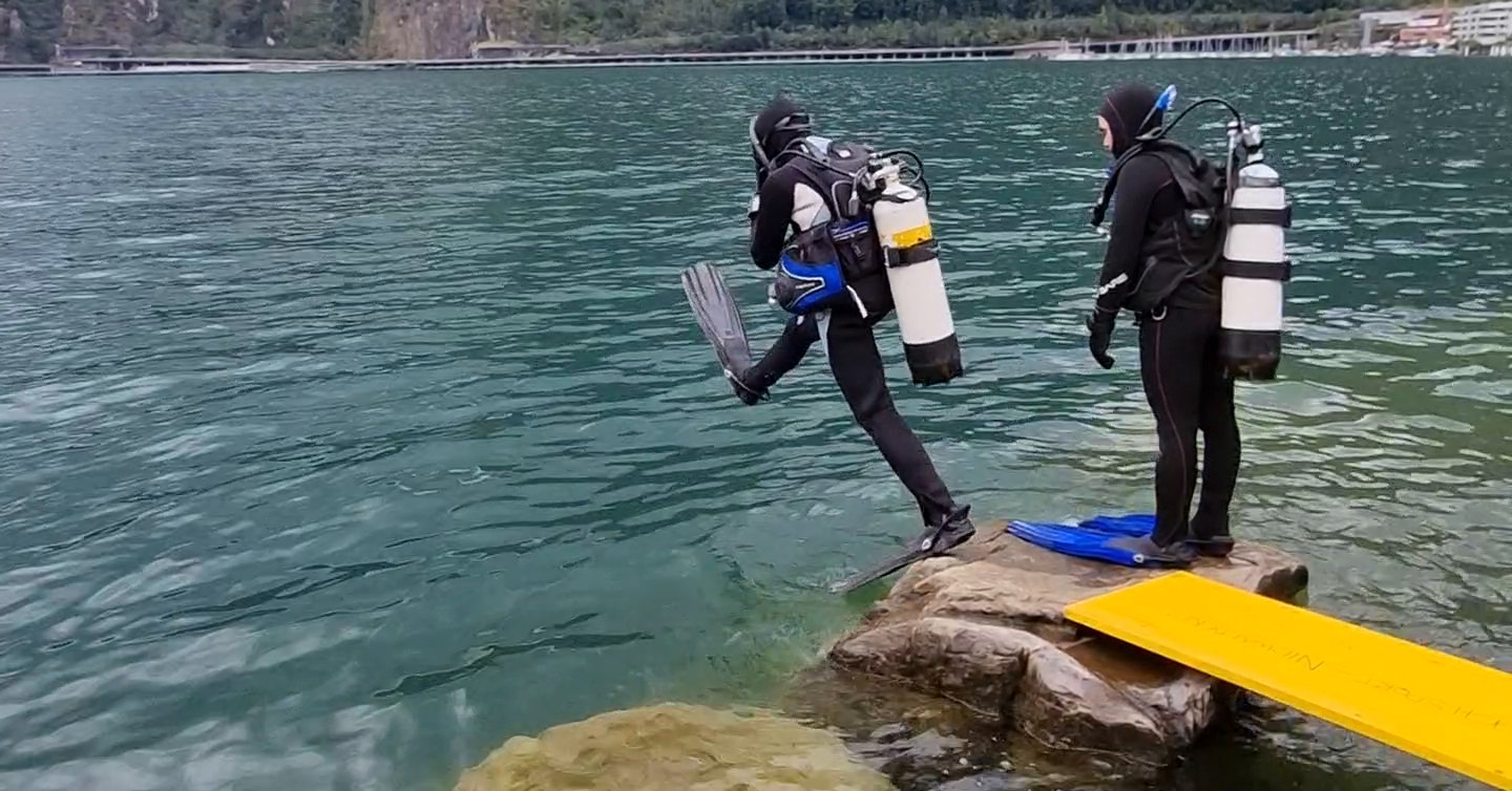 Taucher macht am Ende der gelben Planke einen grossen Schritt ins Wasser, ein Bein noch in der Luft.