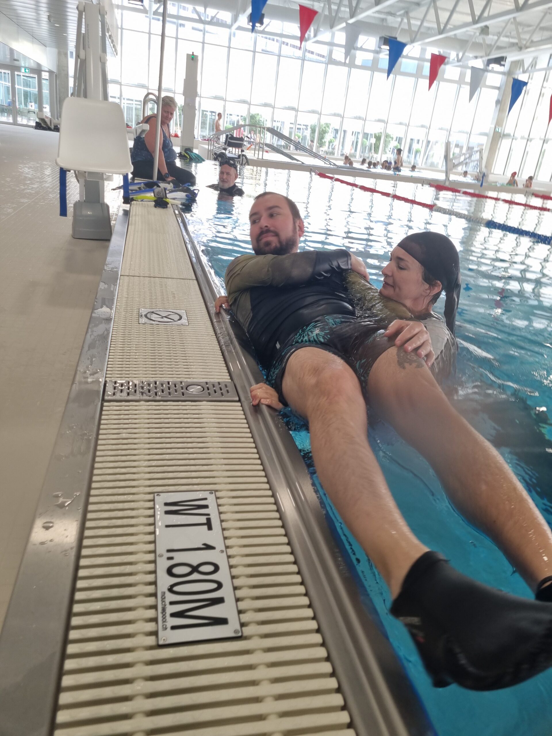 Ein Tauchlehrer gleitet vom Beckenrand ins Wasser, eine Kollegin sichert ihn von der Wasserseite.