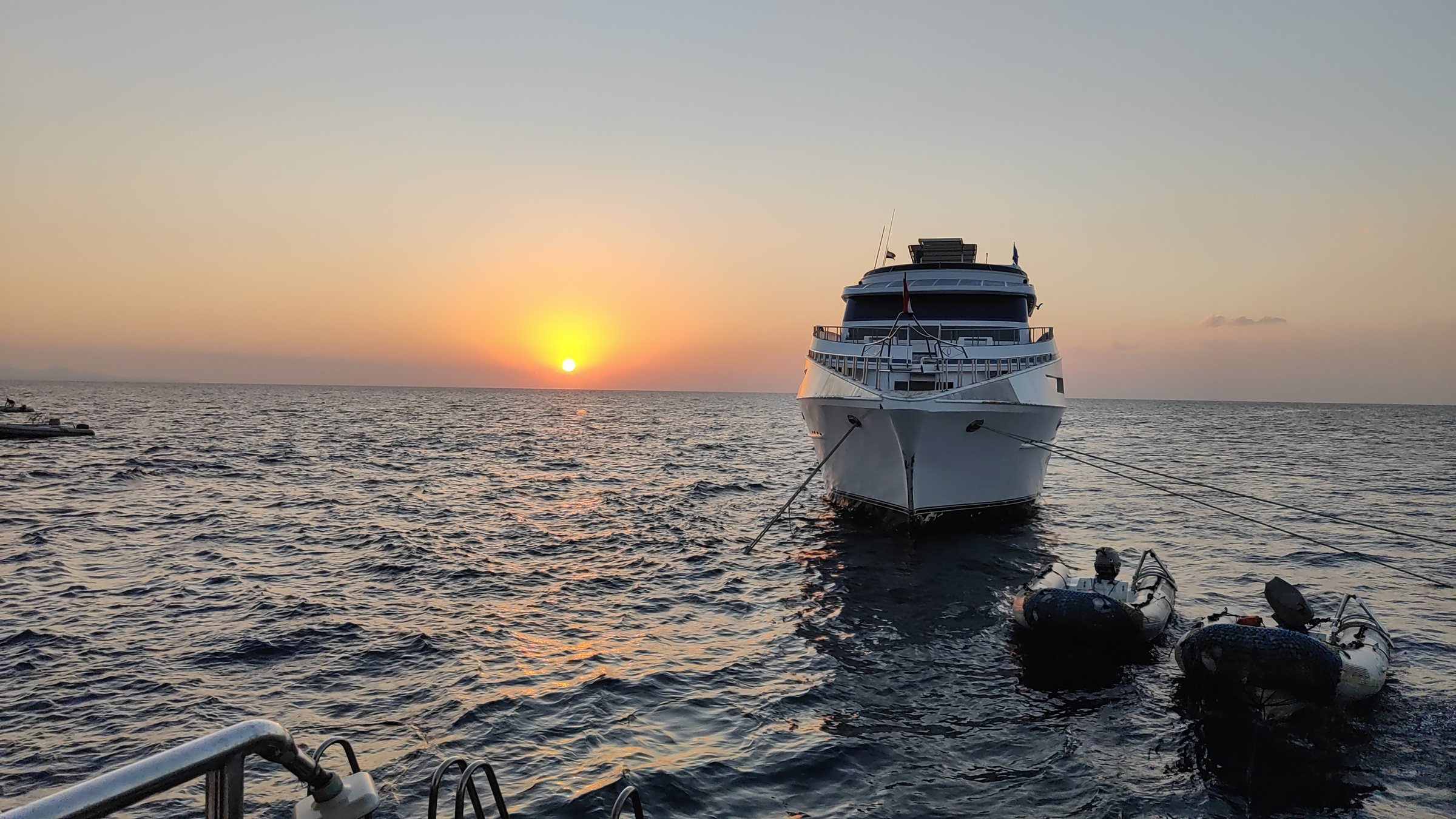 Tauchschiff liegt bei Sonnenuntergang vor Anker auf offenem Meer, im Vordergrund zwei Beiboote
